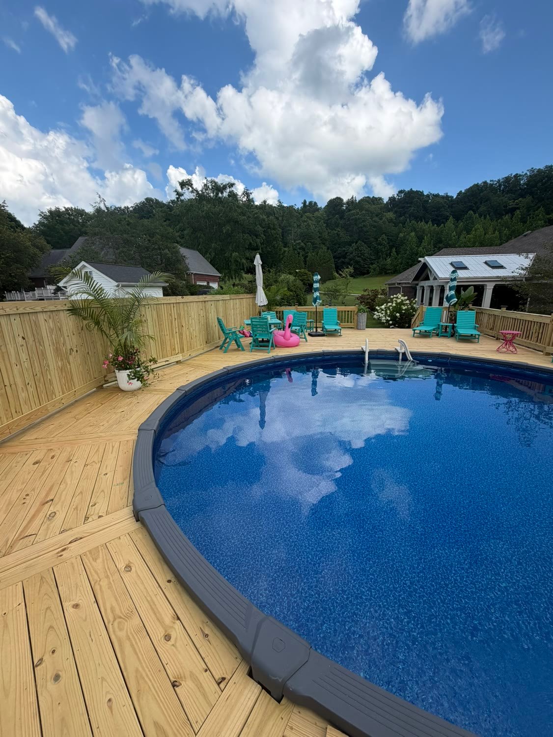 The finished pool deck with railings, a privacy fence and furniture set out around the water.