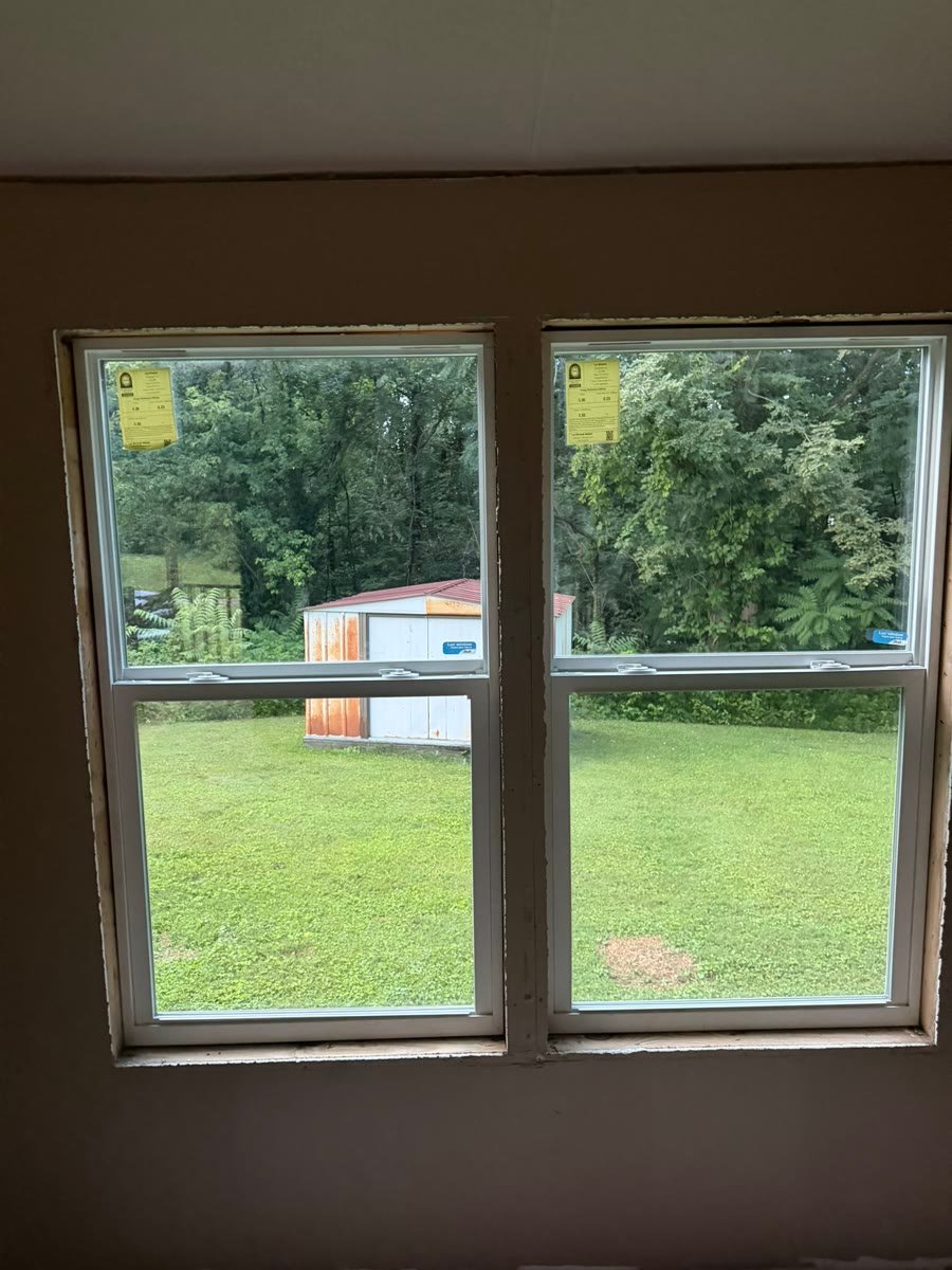 A pair of newly fitted double hung windows seen from inside a room, looking out over a lawn.